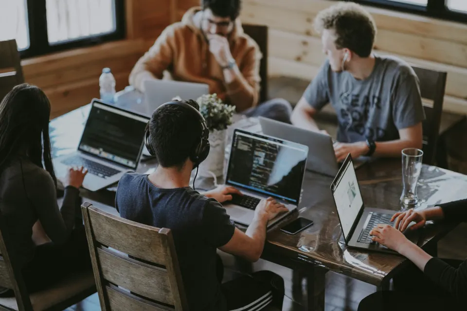 Personas colaborando en una mesa de trabajo con computadoras portátiles
